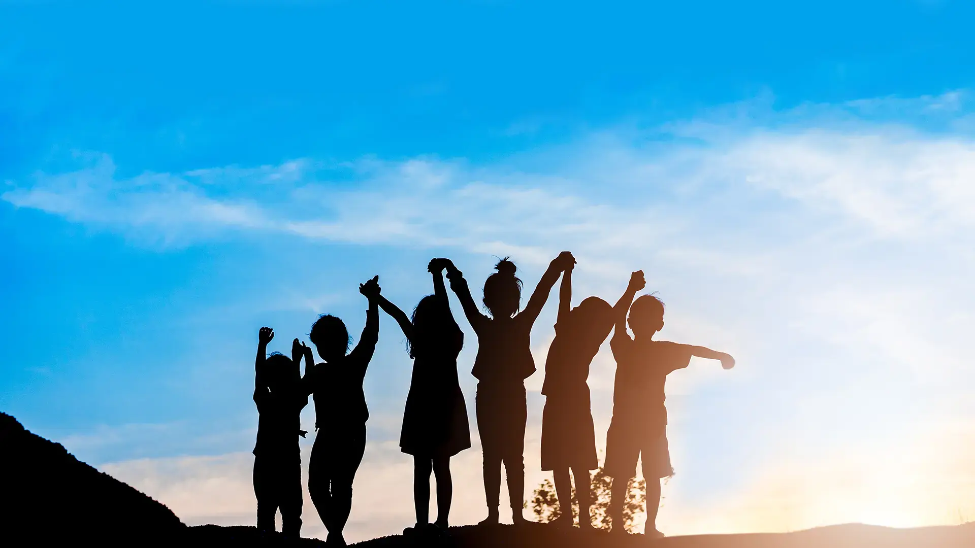 Children standing in a line and holding hands. Sunset in the background.